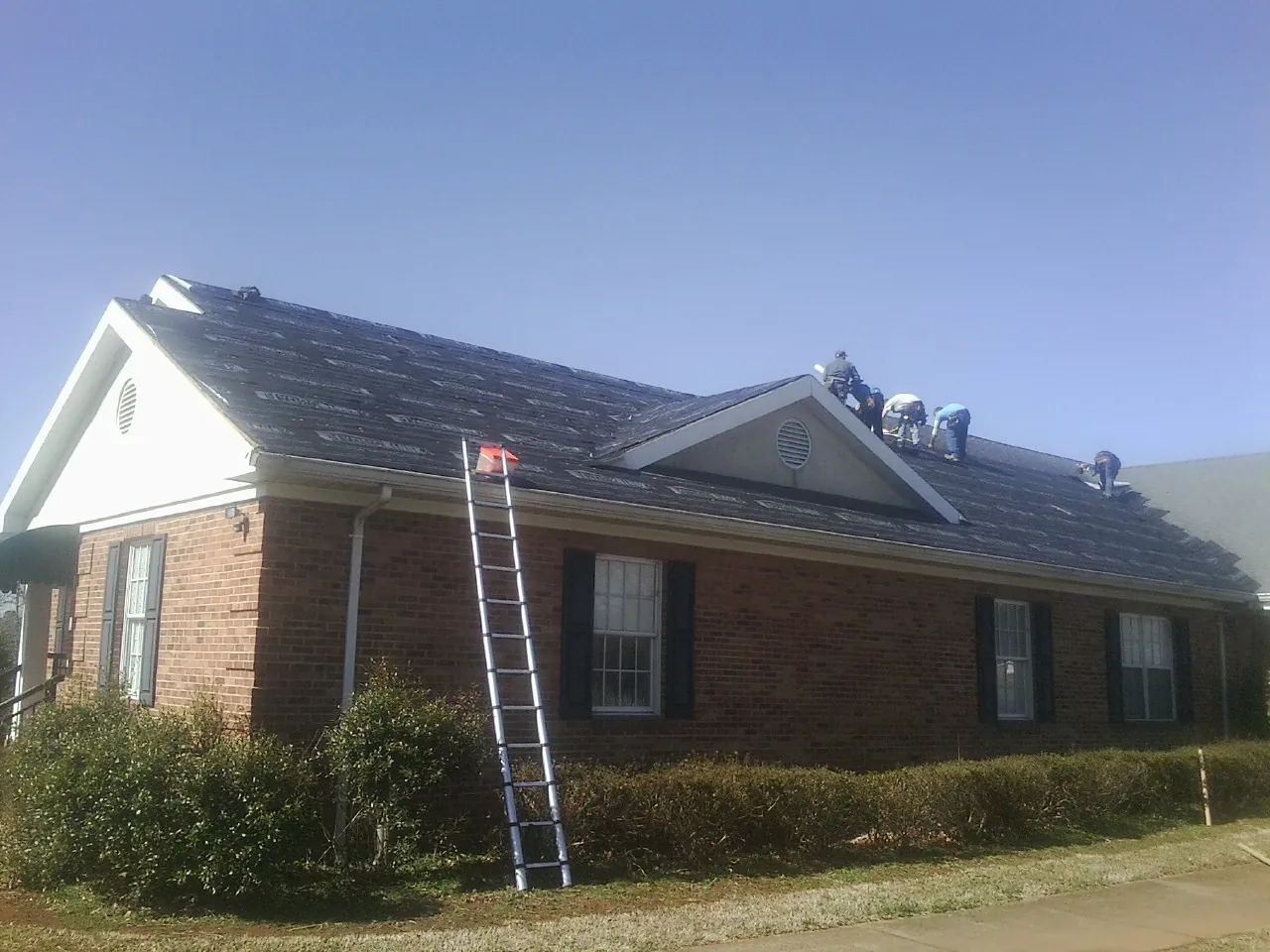 Crew tearing shingles off a brick ranch roof with a ladder set — Emergency Roof Repair work by our crew in Amston