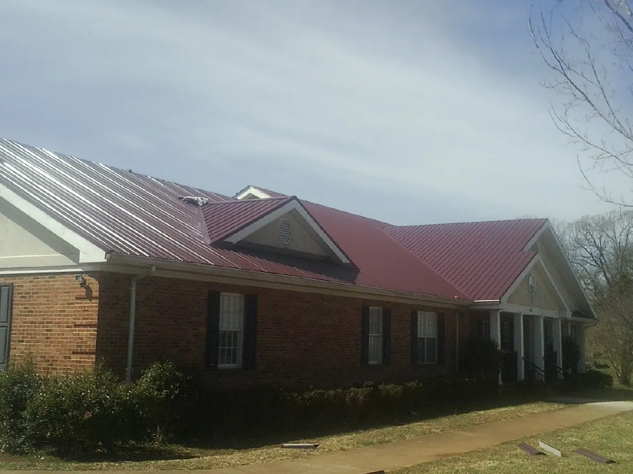Red metal roof with gabled entries on a long brick building, from a Hail Damage Roof Repair job in Amston