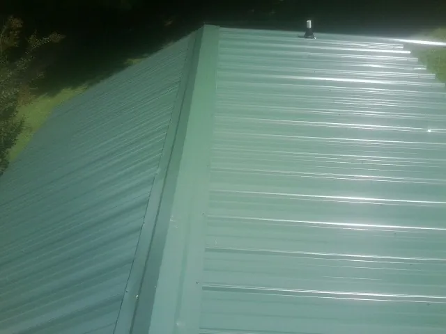 New green metal panels meeting at the ridge of a roof — Flat Roof Repair work by our crew in Amston