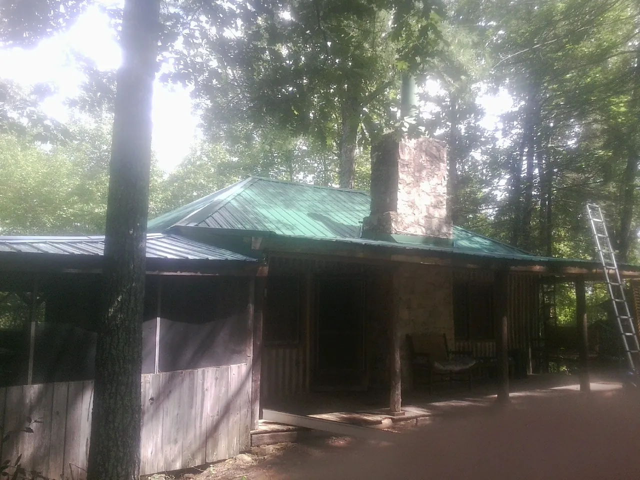 Green metal roof and stone chimney above a log cabin porch in Amston