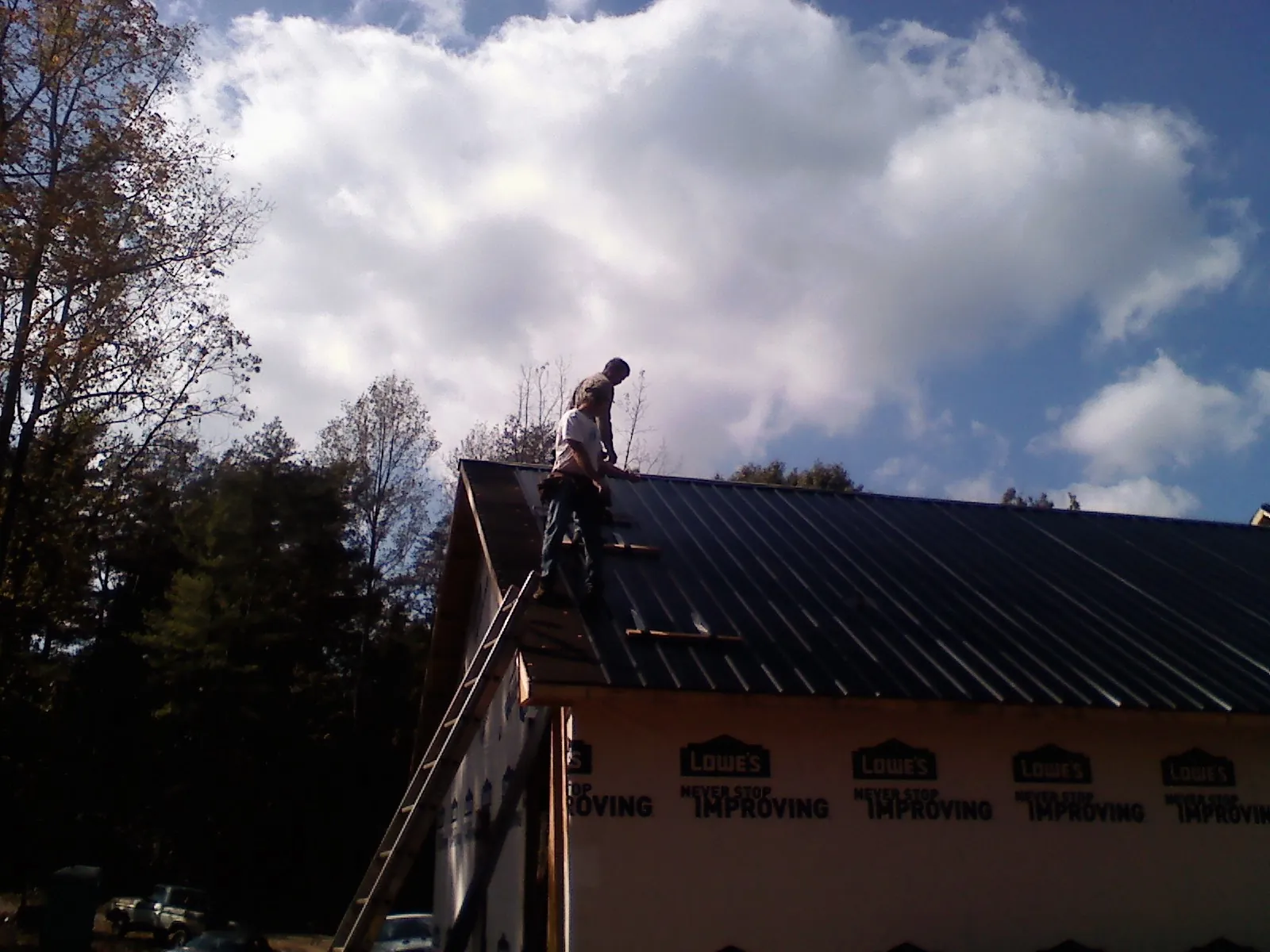 Roofer fastening dark metal panels high against a cloudy sky, from a Roof Inspection job in Amston