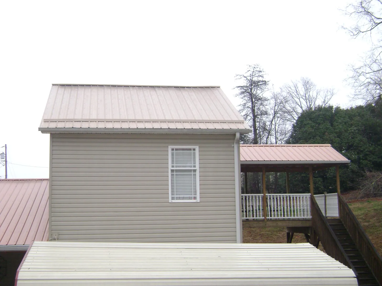 Tan metal roofs on a two story addition and attached porch, from a Roof Replacement job in Amston